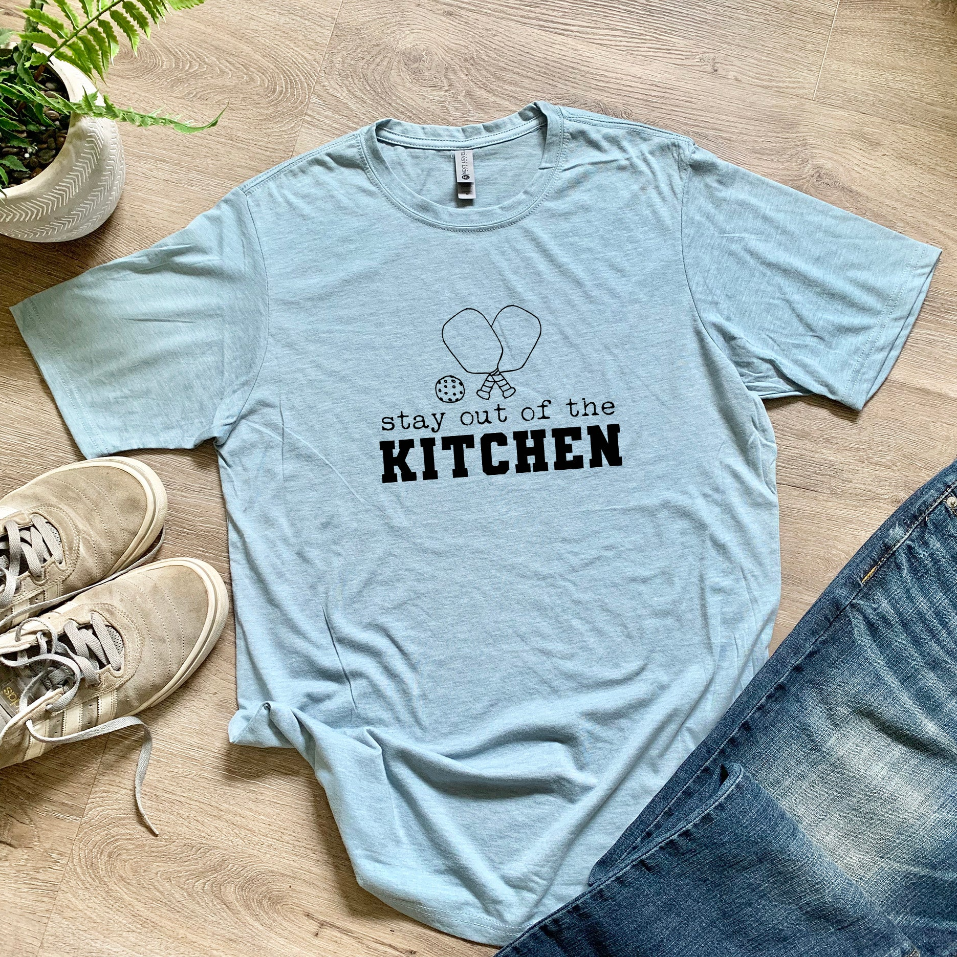 a t - shirt that says stay out of the kitchen next to a pair of