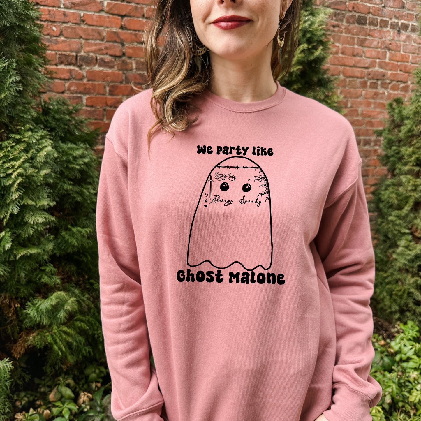 a woman standing in front of a brick wall wearing a pink sweatshirt