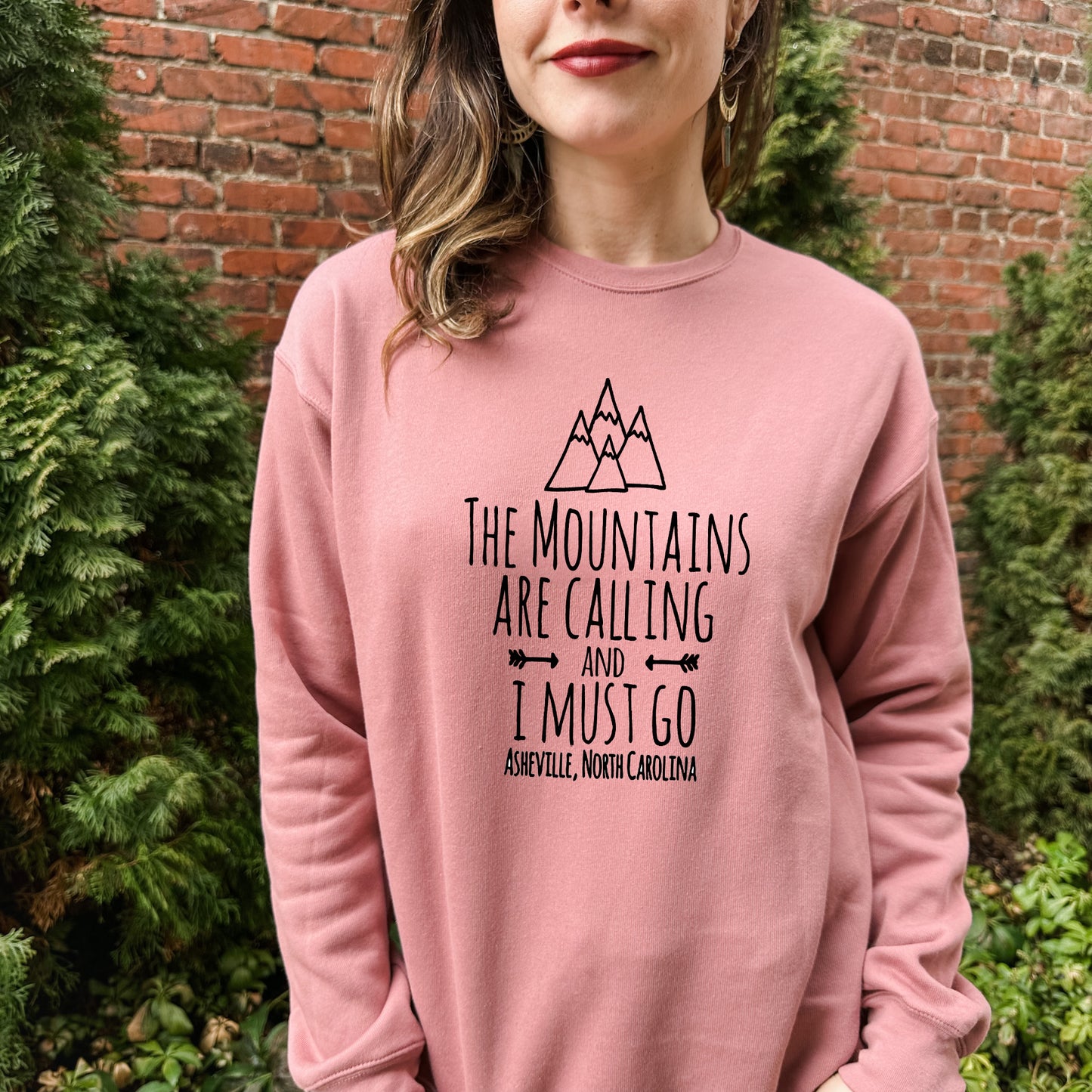 a woman wearing a pink sweatshirt that says the mountains are calling and i must go