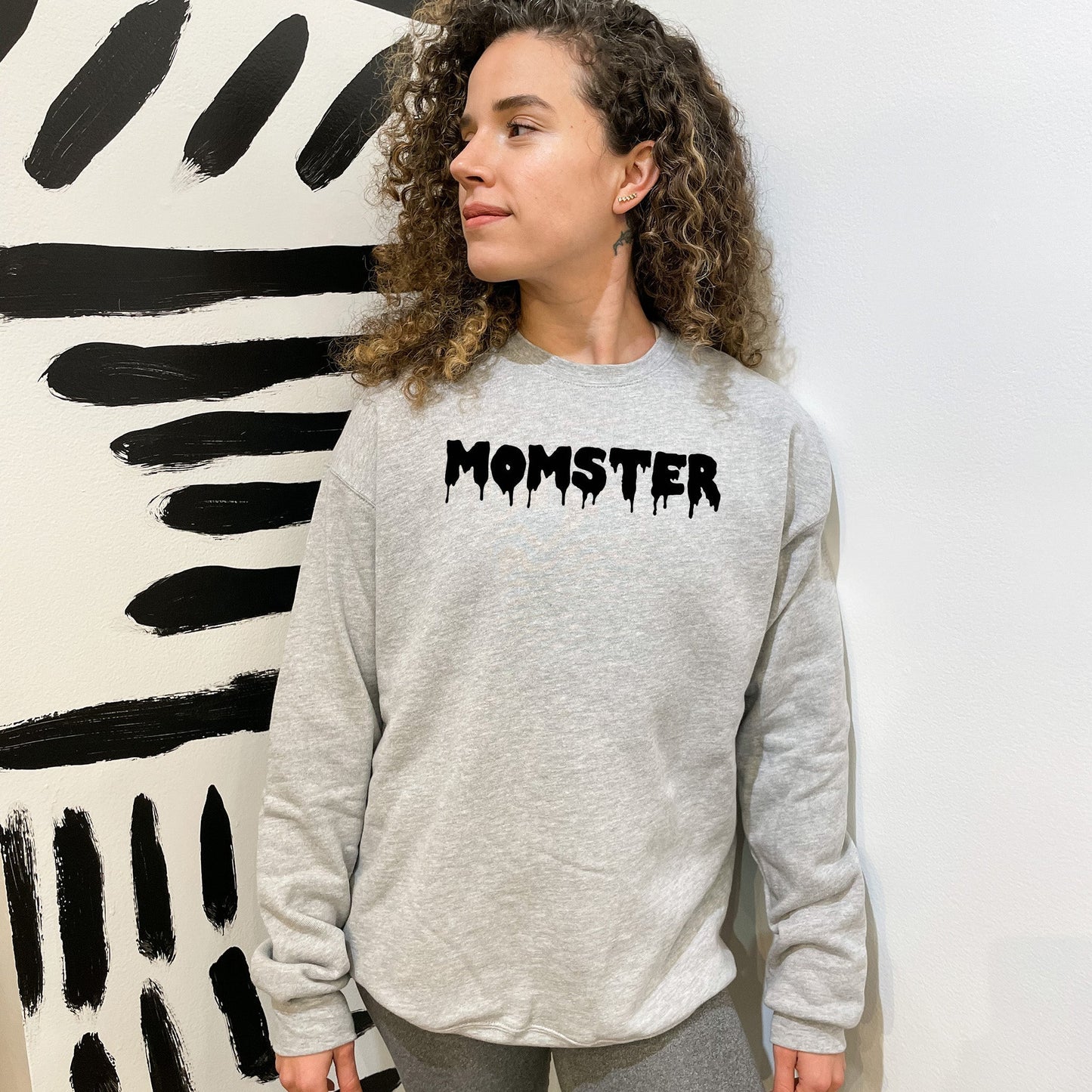 a woman standing in front of a painting with the word monster on it