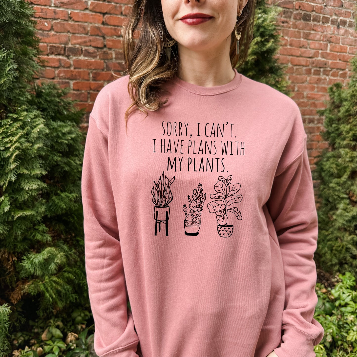 a woman wearing a pink sweatshirt that says sorry i can't i have plants