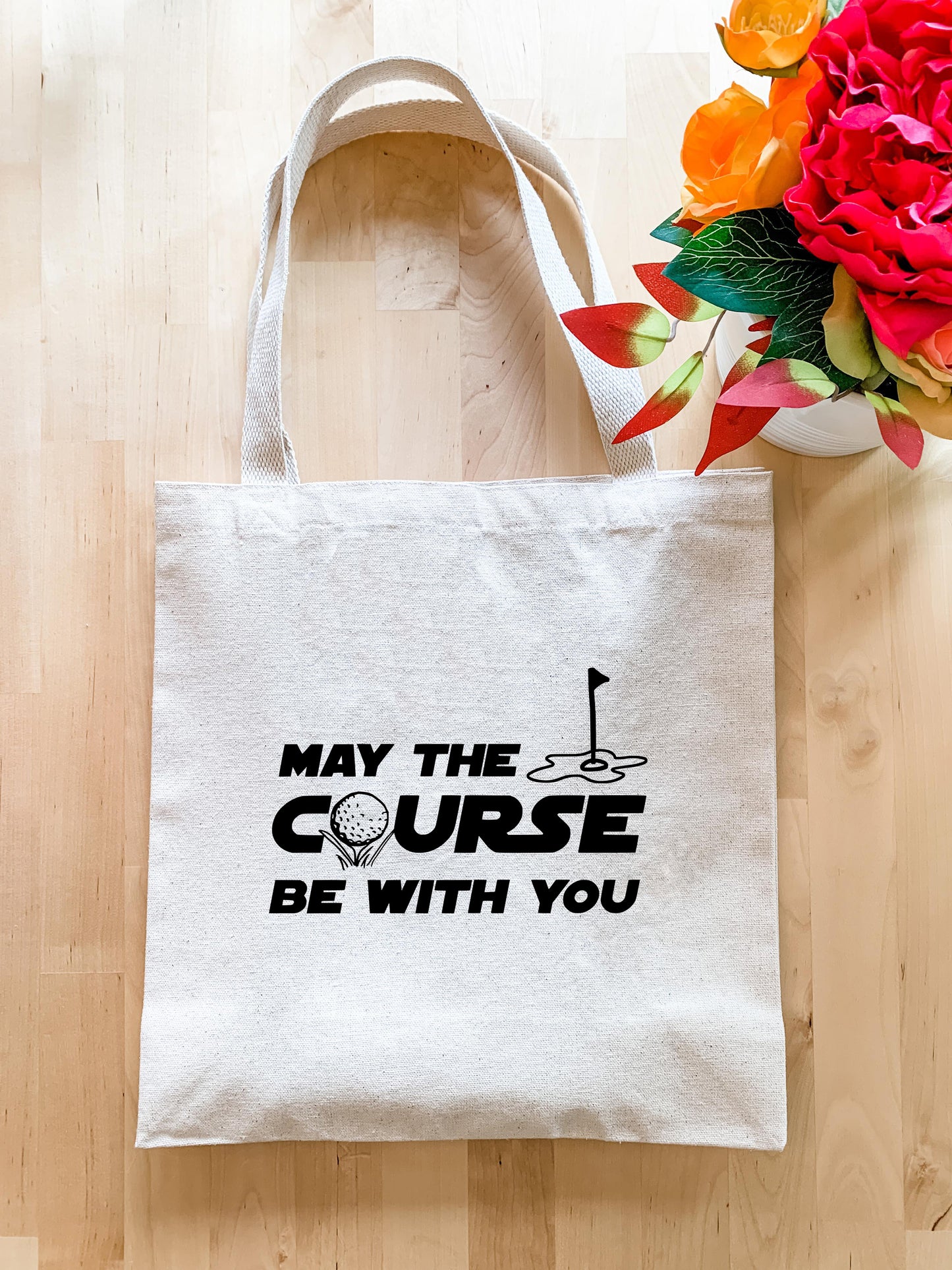 a tote bag sitting on a wooden floor next to a vase of flowers