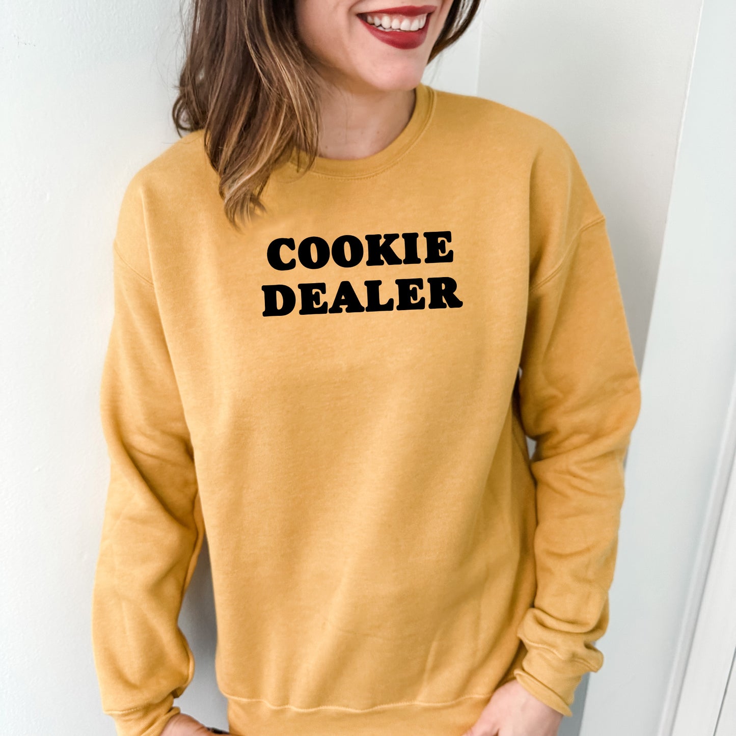 a woman wearing a yellow sweatshirt with the words cookie dealer printed on it