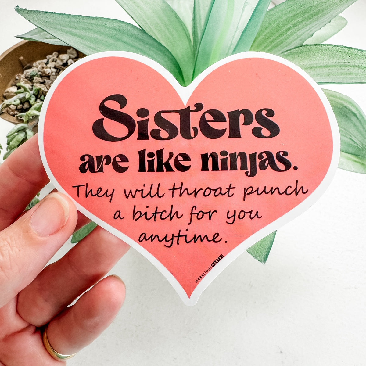 a hand holding a heart shaped sticker that says sisters are like ninjas