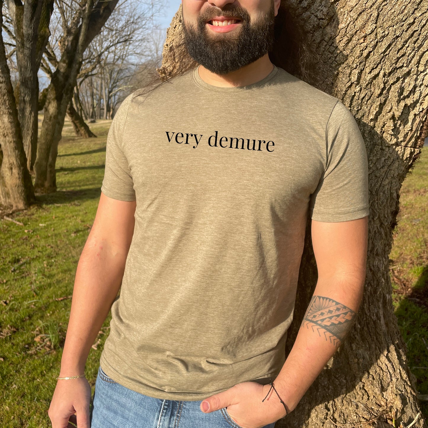 a man standing in front of a tree wearing a very demure t - shirt