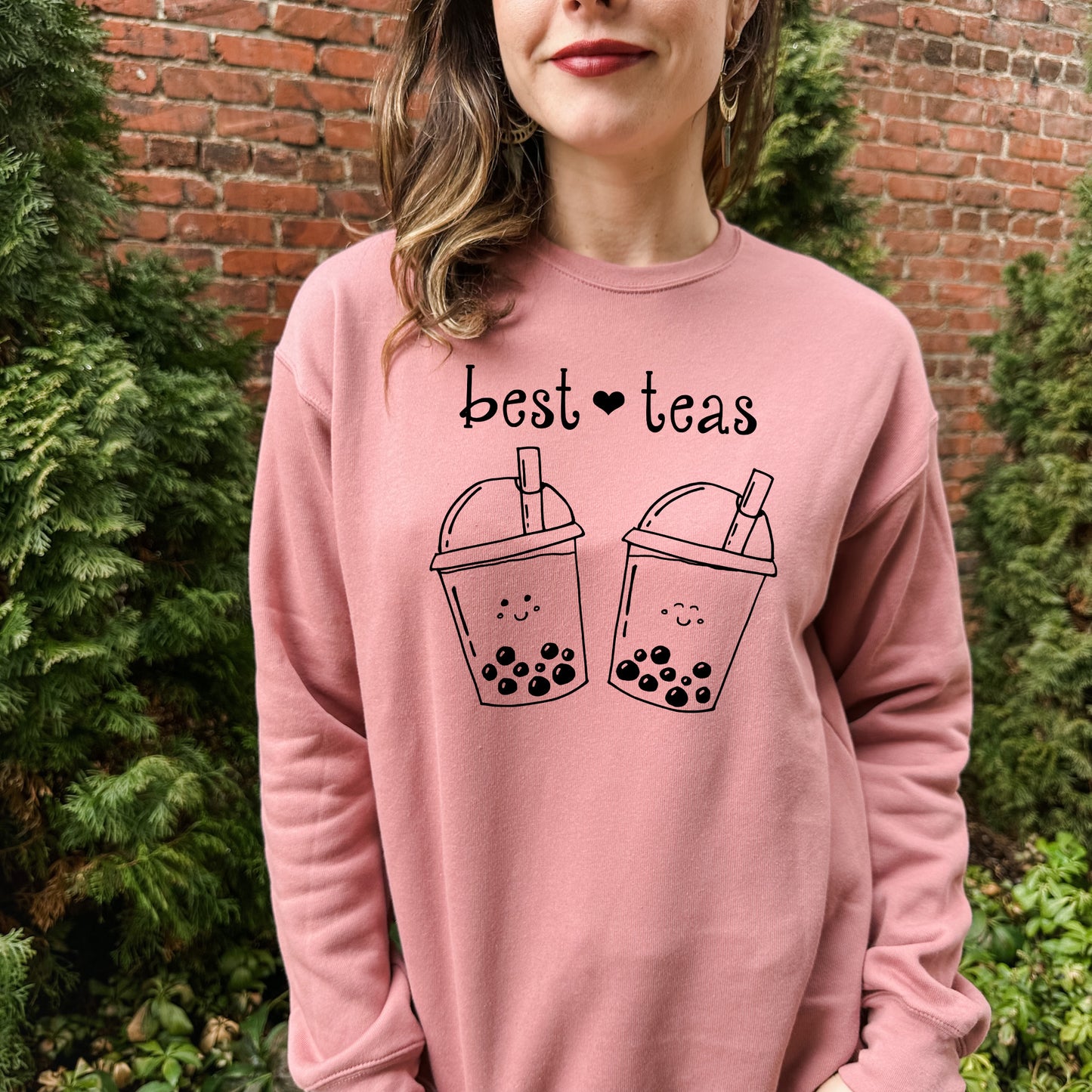 a woman wearing a pink sweatshirt that says best teas