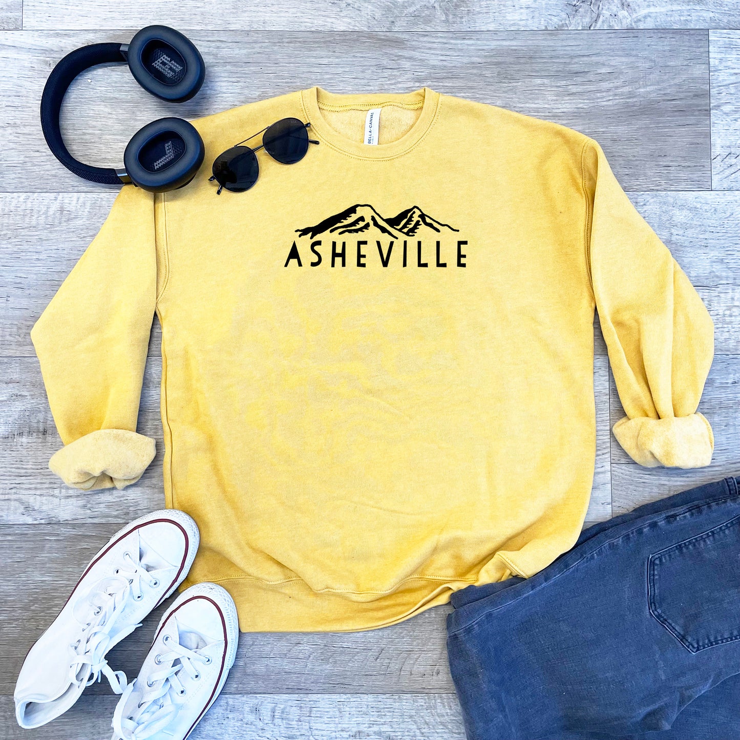 a sweatshirt, headphones, and pair of jeans on a wooden floor