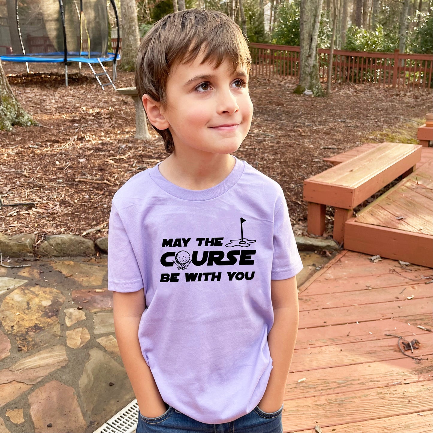 a young boy standing on a deck wearing a purple shirt