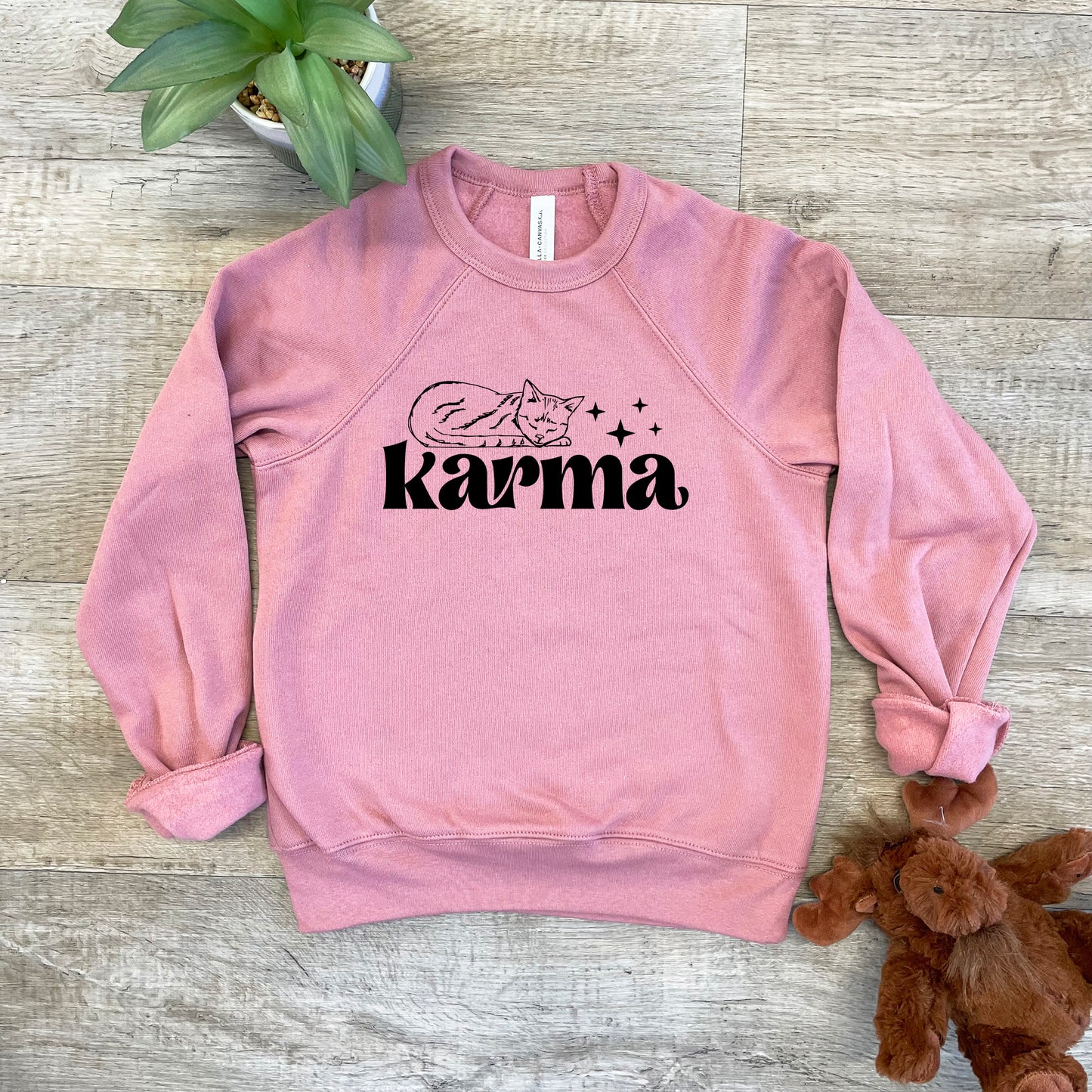 a pink sweatshirt with the word karma on it next to a teddy bear