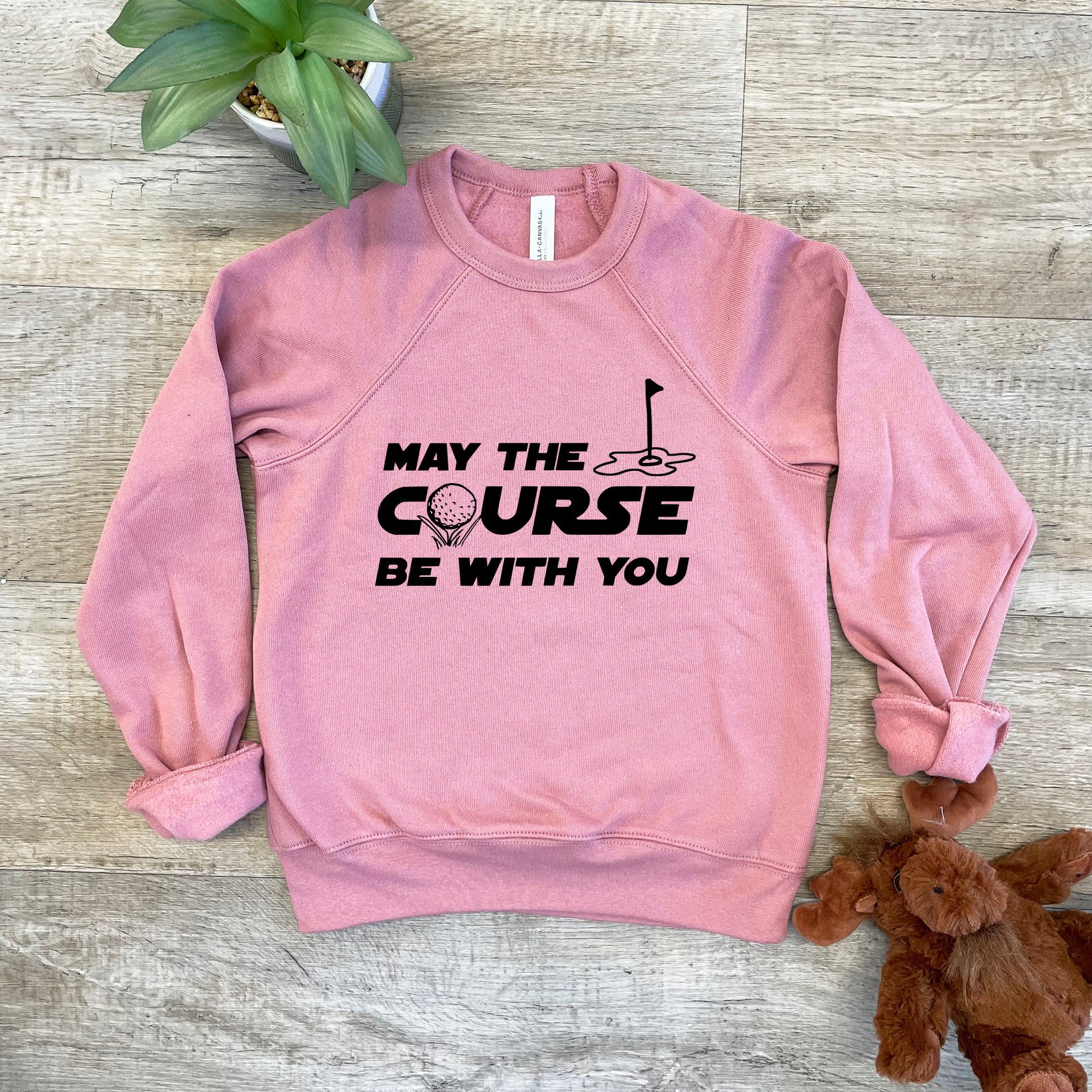 a pink sweatshirt that says may the course be with you next to a teddy bear