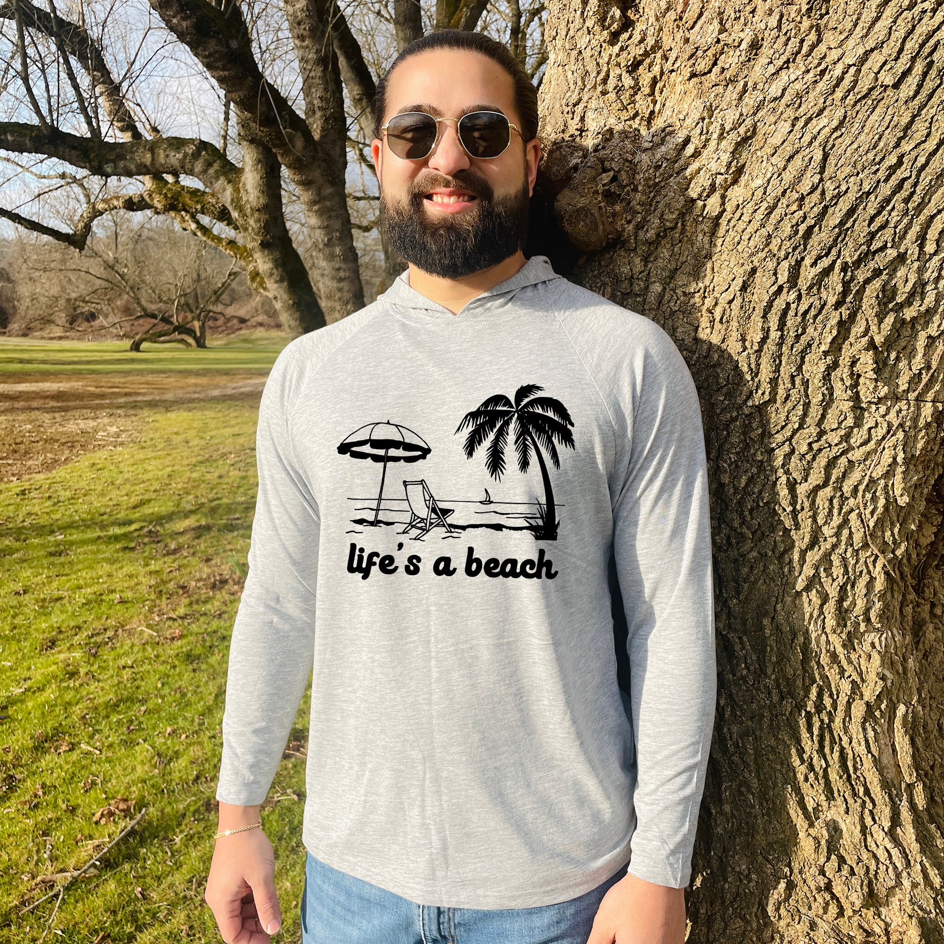 a man standing next to a tree wearing a shirt that says life's a