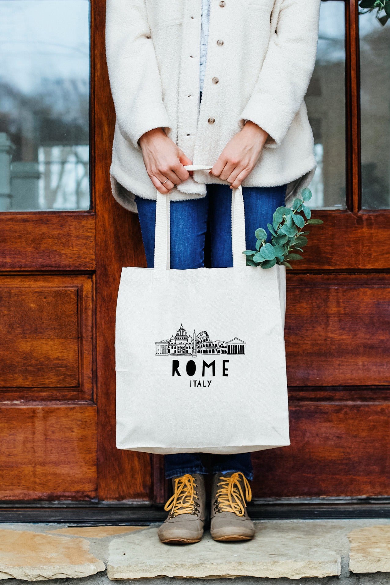 a woman holding a white tote bag in front of a door