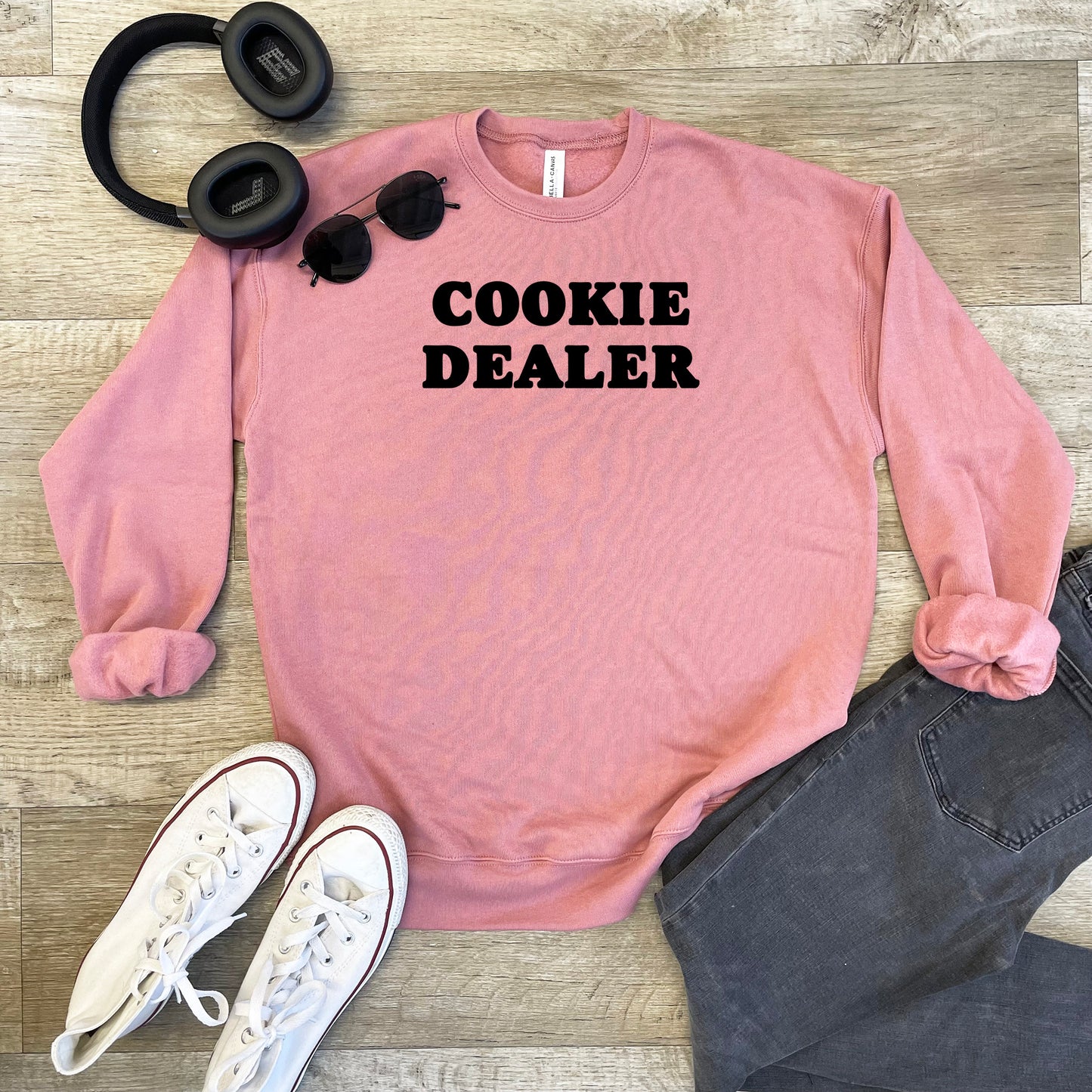 a pink sweatshirt that says cookie dealer next to headphones