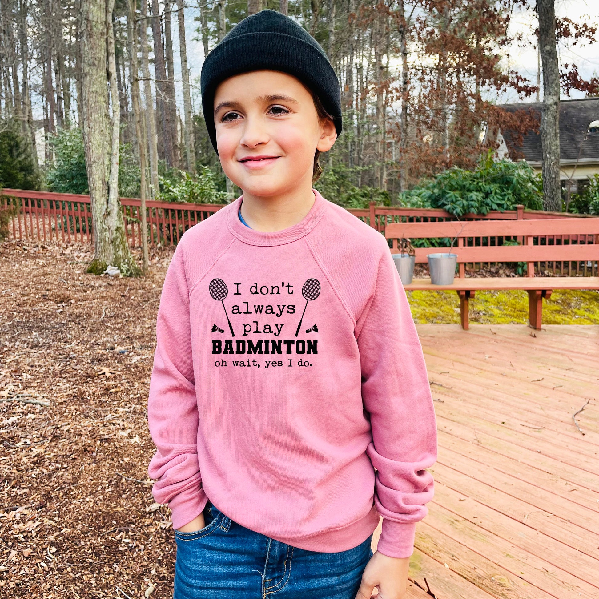 a young boy standing on a deck wearing a pink sweatshirt