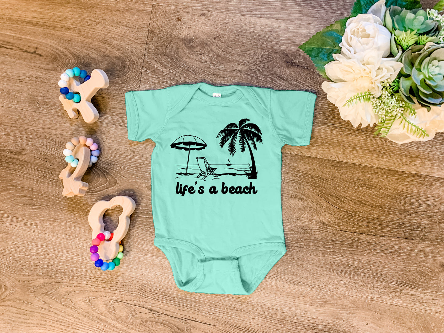 a baby bodysuit that says life's a beach next to a pair of