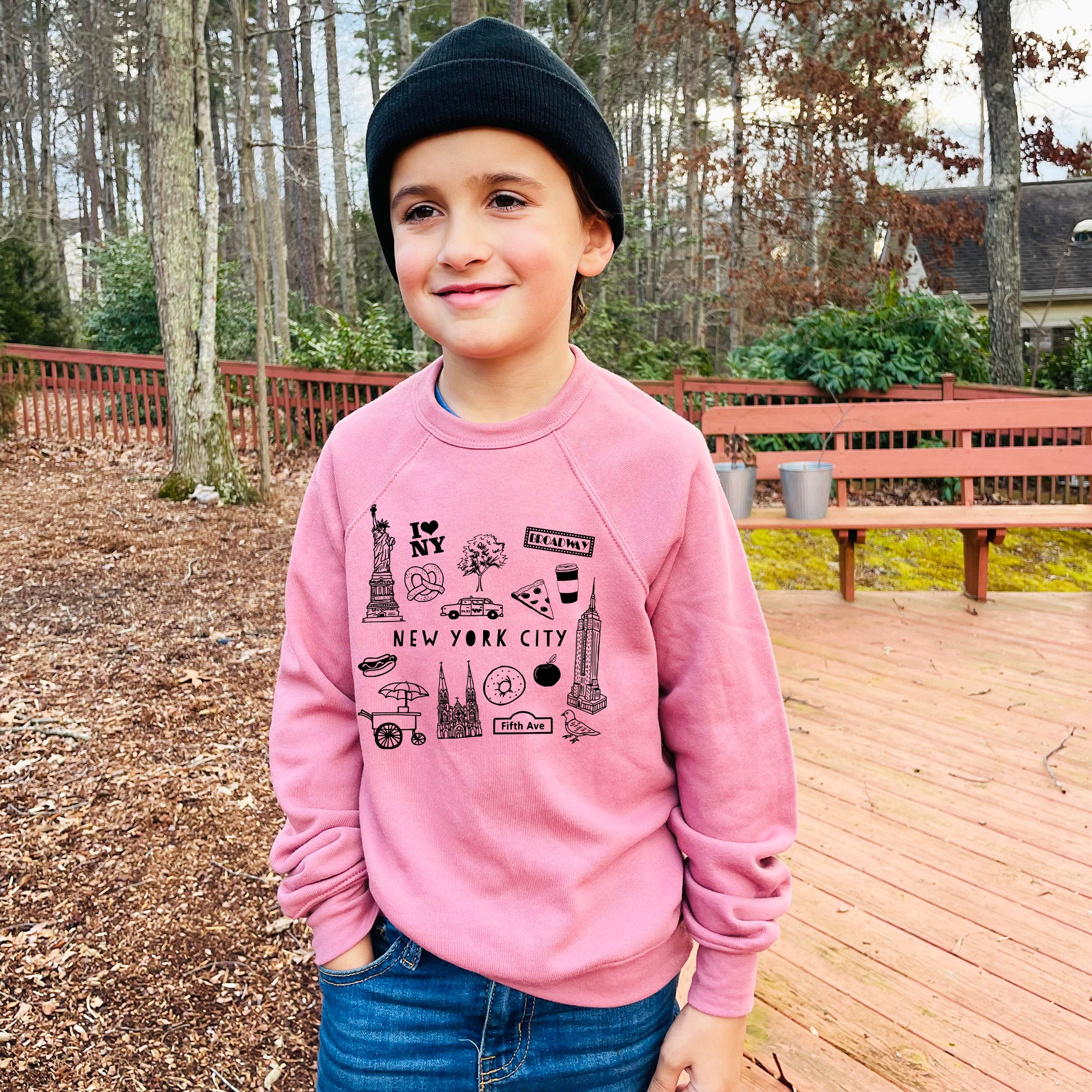 a young boy standing on a deck wearing a pink sweatshirt