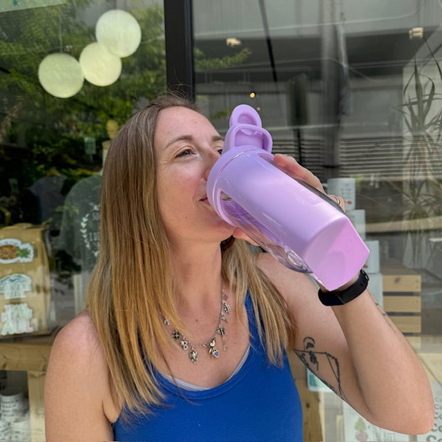 a woman drinking out of a purple water bottle