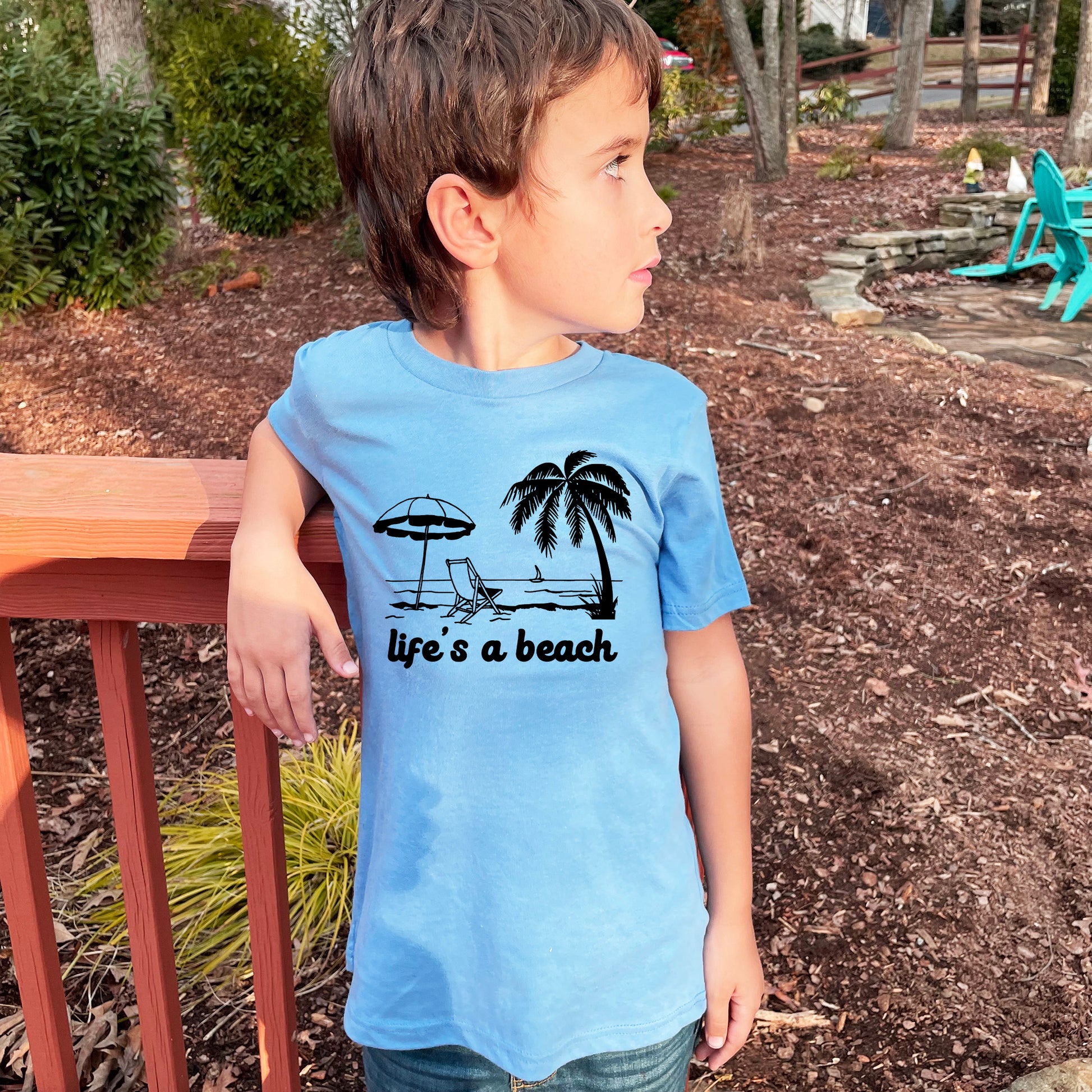 a young boy standing on a wooden deck next to a palm tree