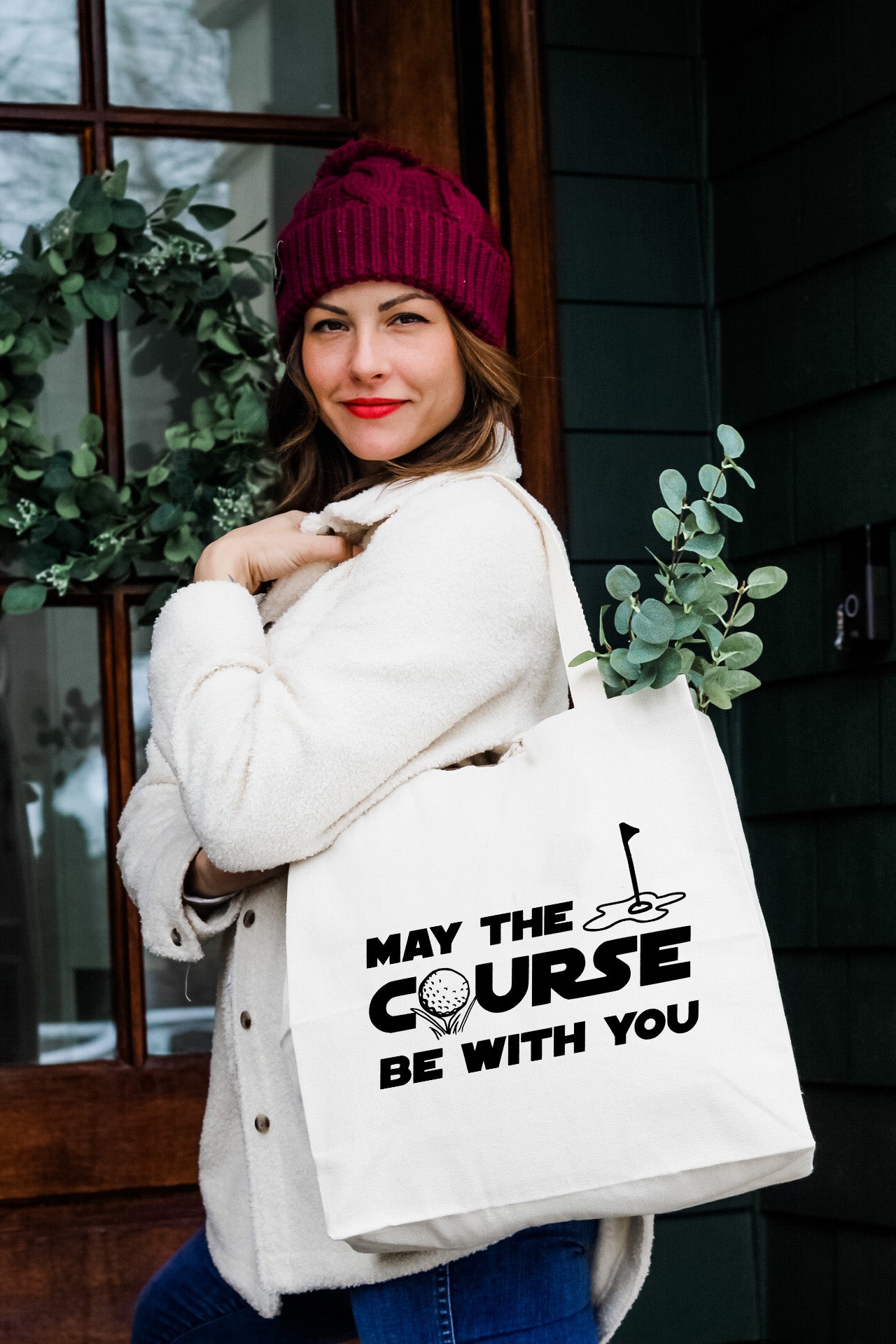 a woman carrying a white tote bag that says may the course be with you