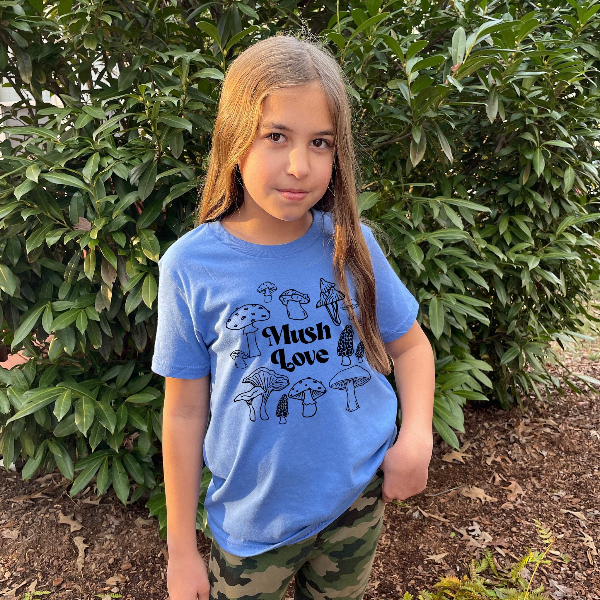 a young girl standing in front of a bush