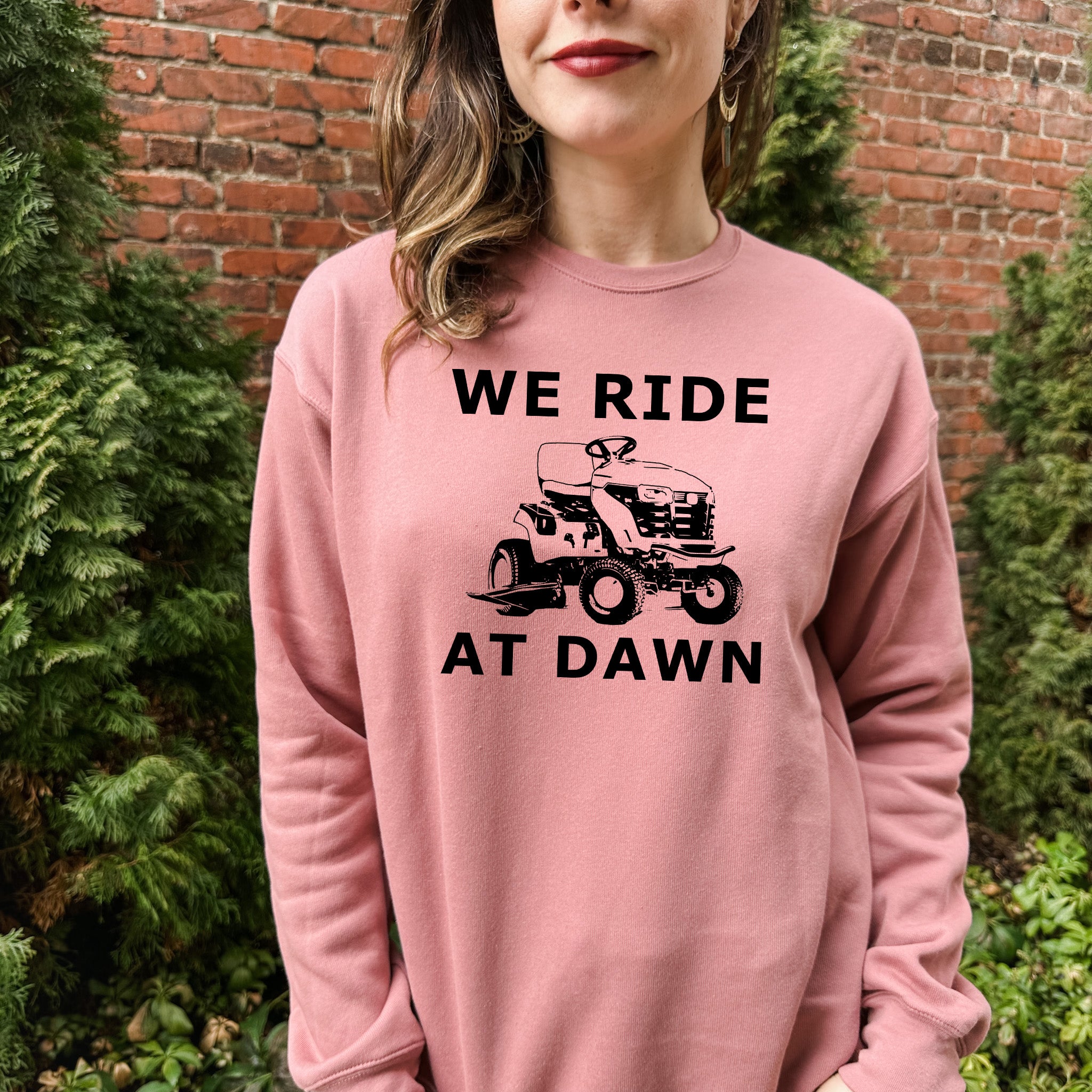 a woman wearing a pink sweatshirt that says we ride at dawn