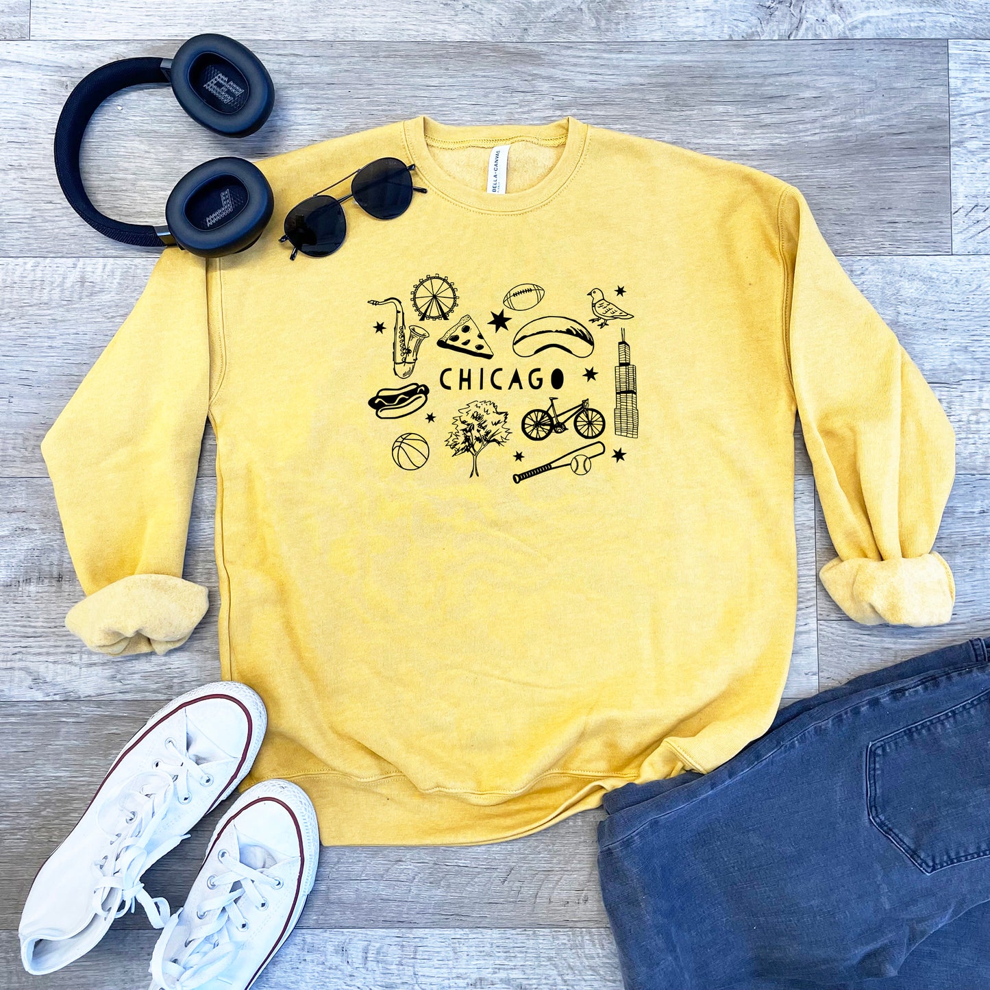 a yellow chicago sweatshirt, sunglasses, headphones, and a pair of blue jeans