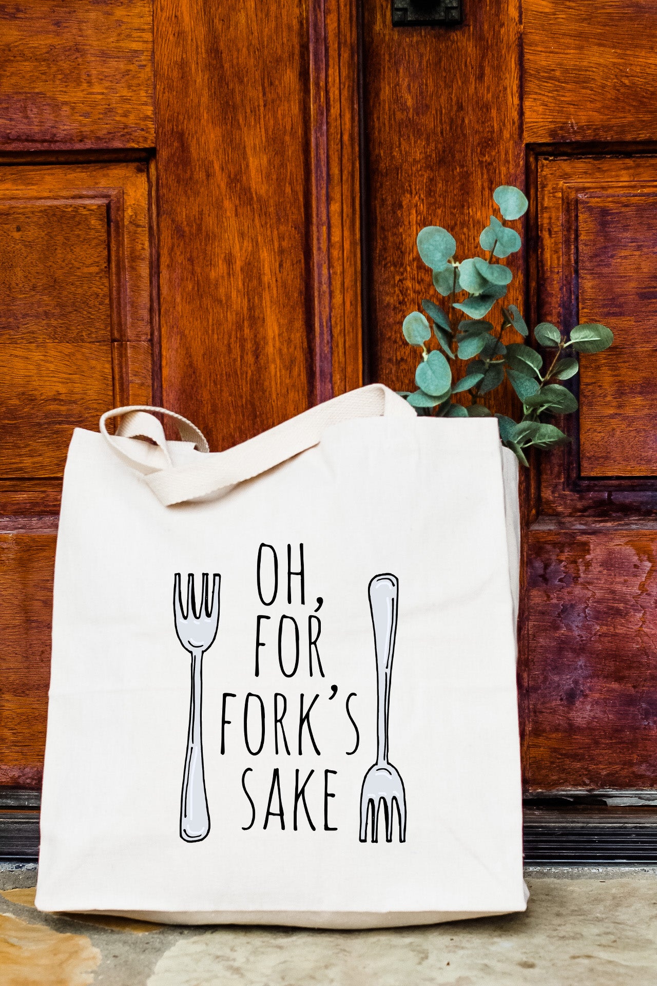 a white tote bag with a fork on it sitting in front of a door
