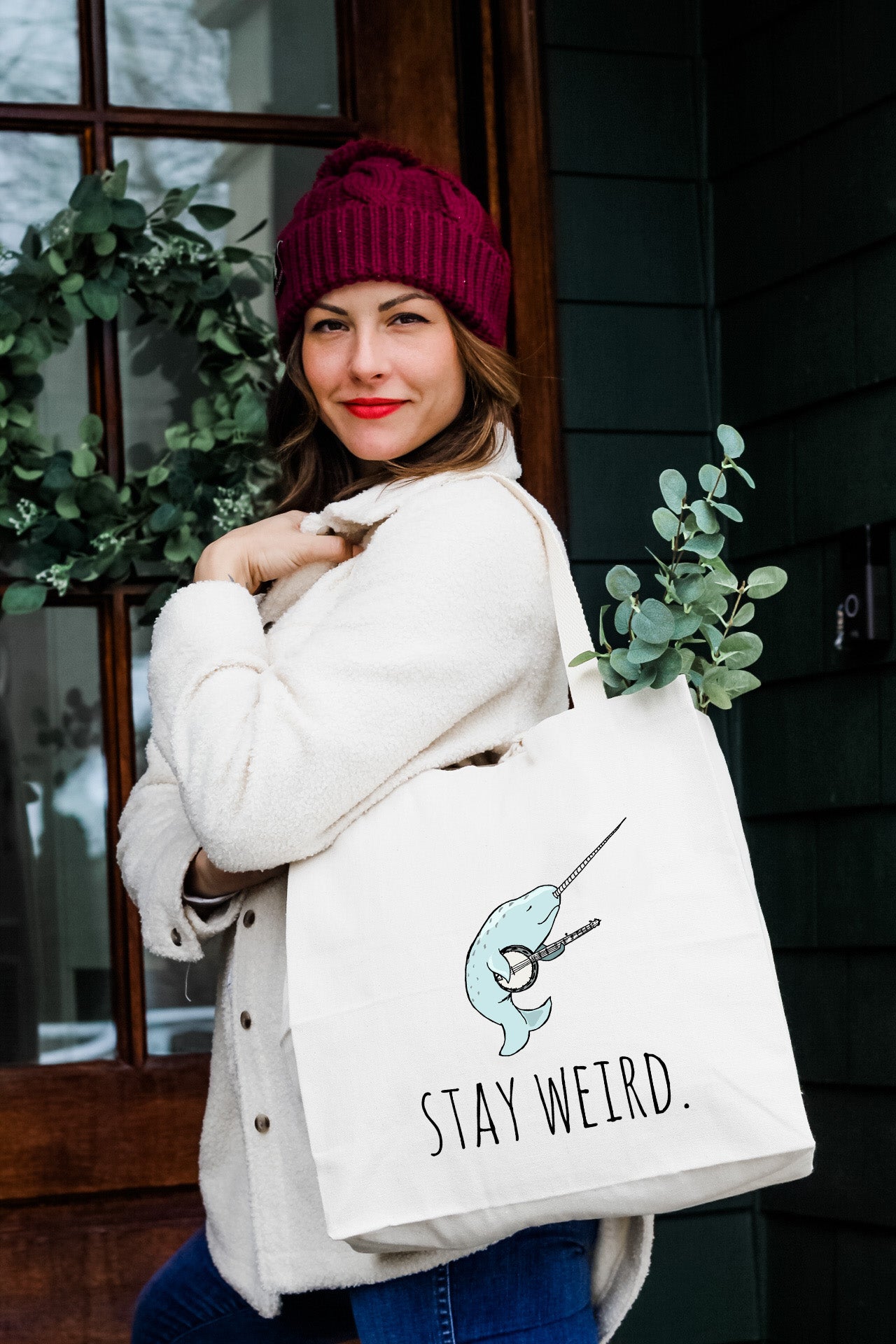 a woman carrying a white tote bag that says stay weird