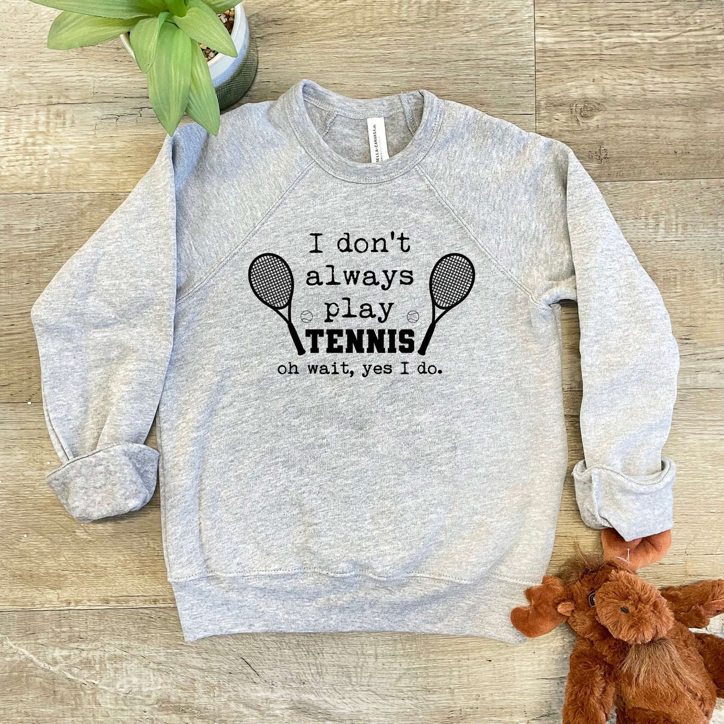 a sweatshirt with a tennis racket on it next to a teddy bear