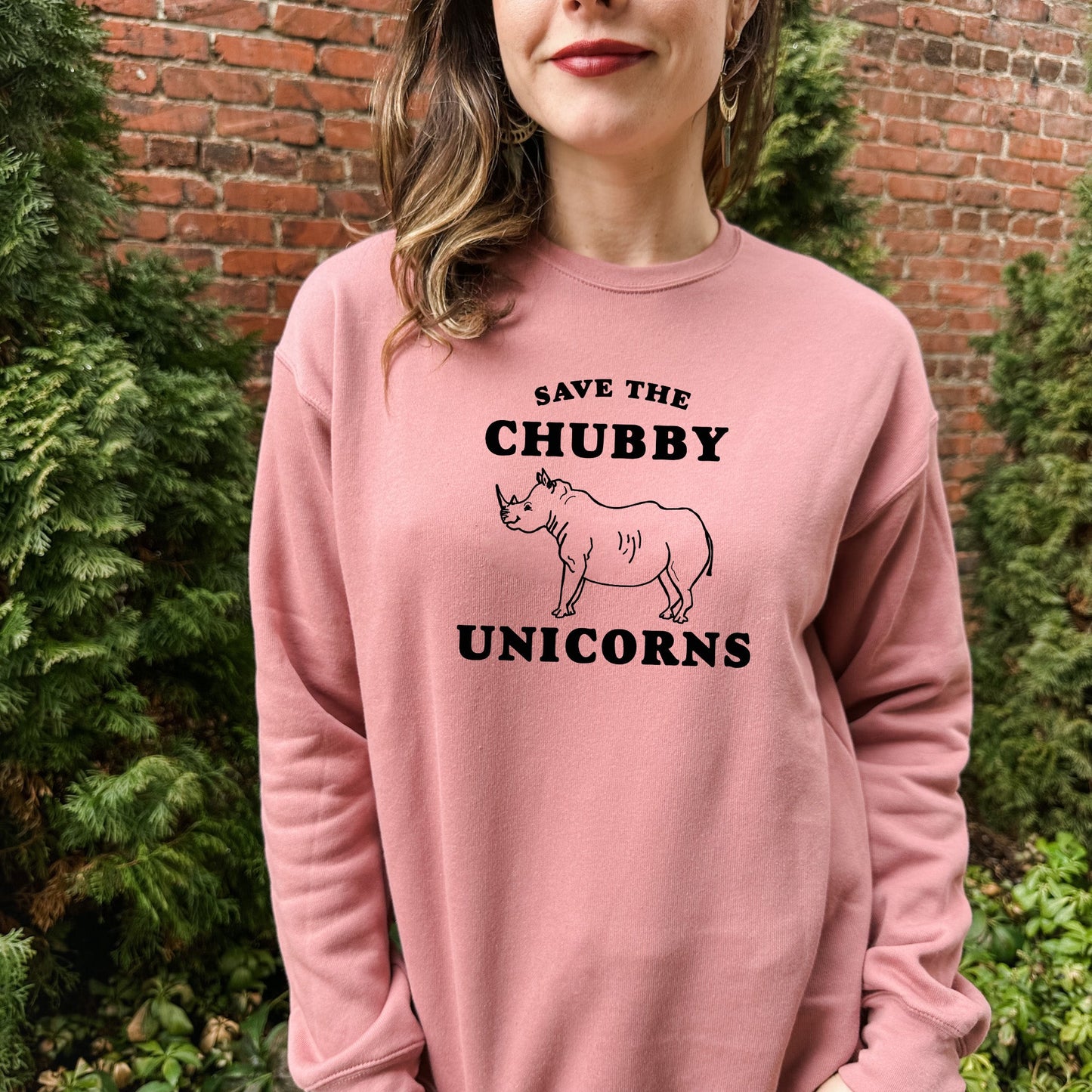 a woman wearing a pink sweatshirt that says save the chubby unicorns