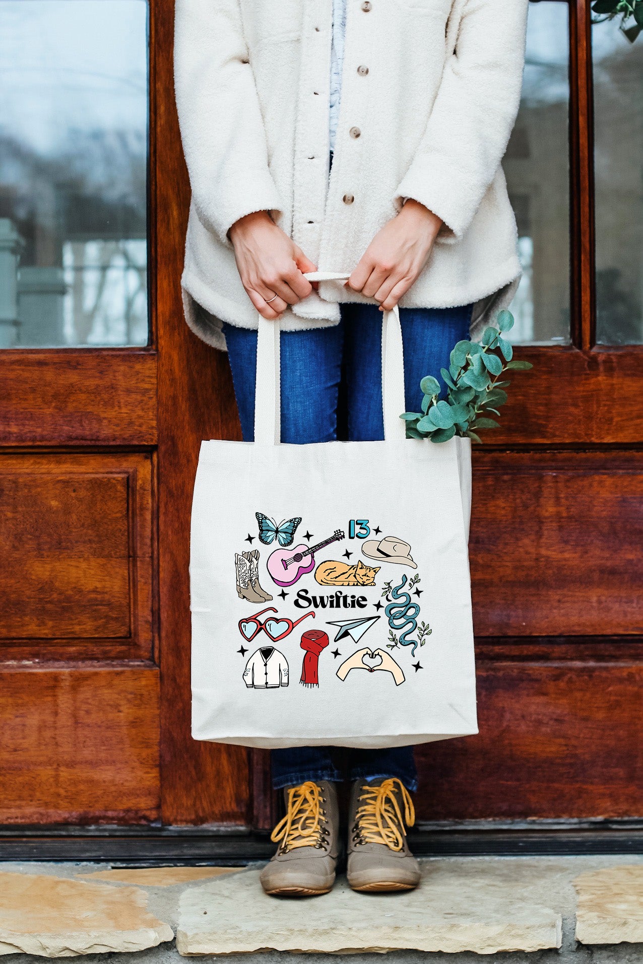 a woman holding a white tote bag in front of a door