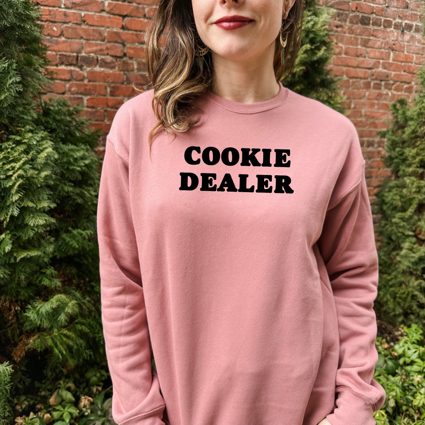 a woman wearing a pink sweatshirt that says cookie dealer