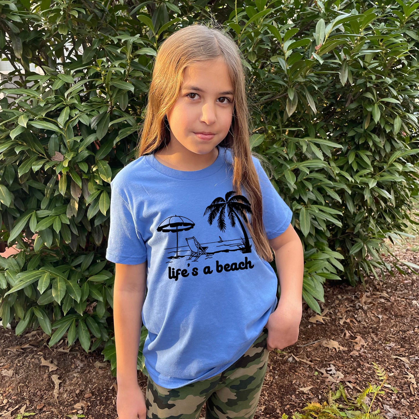 a little girl standing in front of a bush