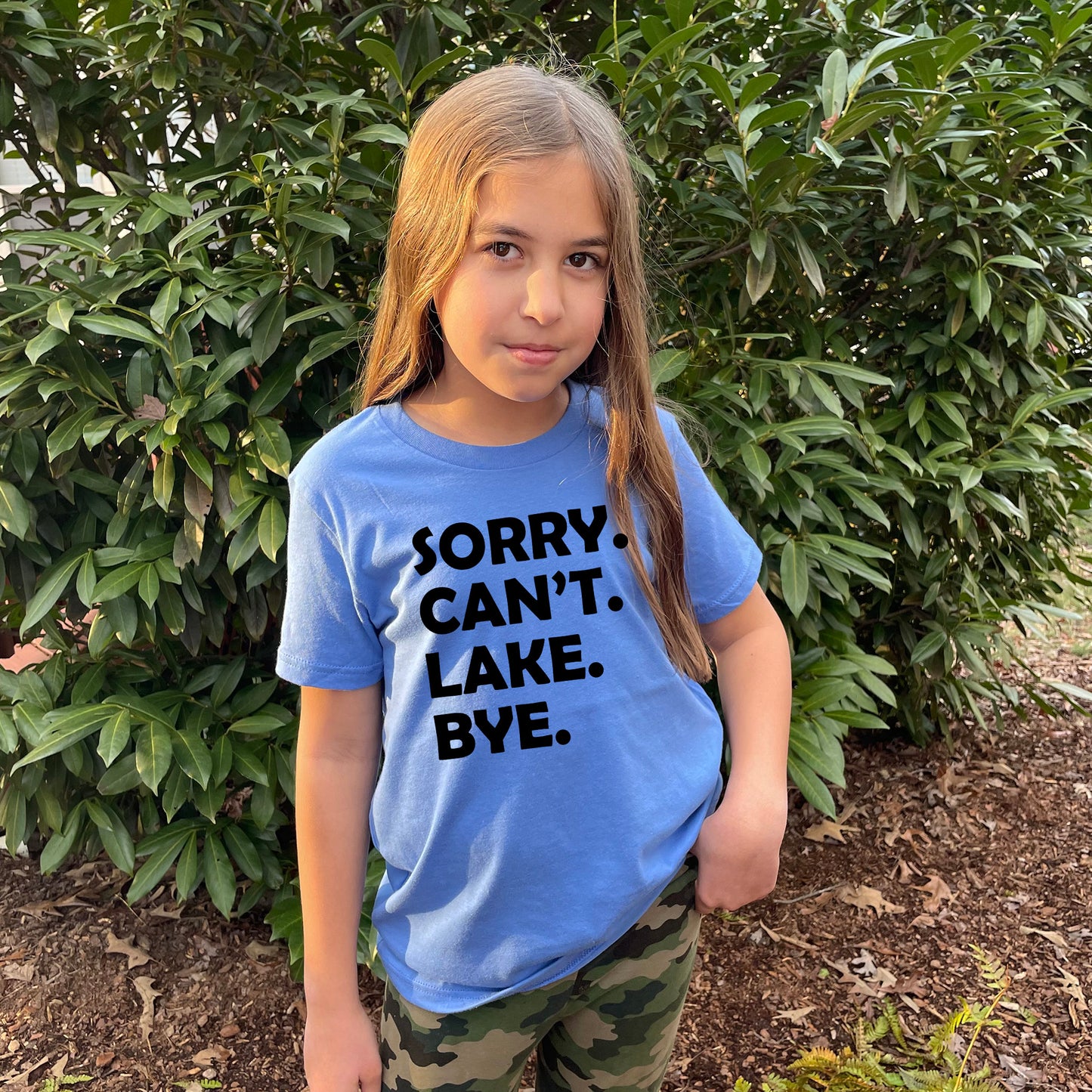 a young girl standing in front of a bush