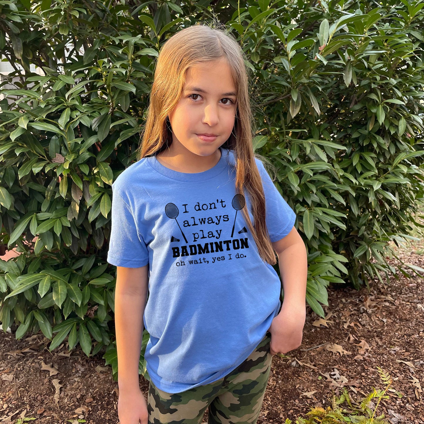 a little girl standing in front of a bush