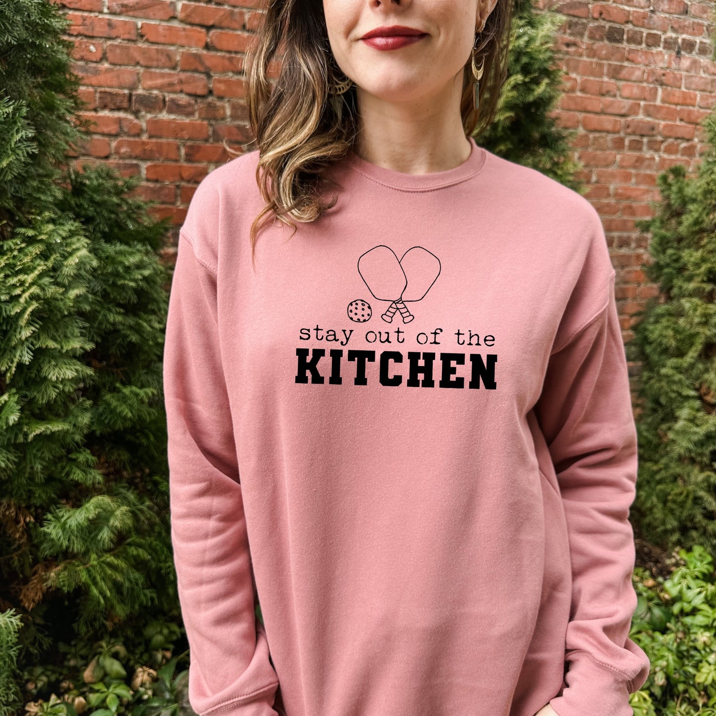 a woman wearing a pink sweatshirt that says stay out of the kitchen