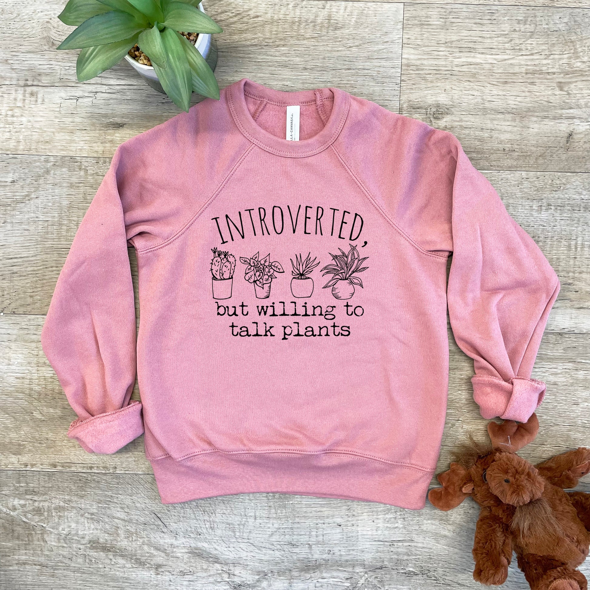 a pink sweatshirt with a plant on it next to a teddy bear