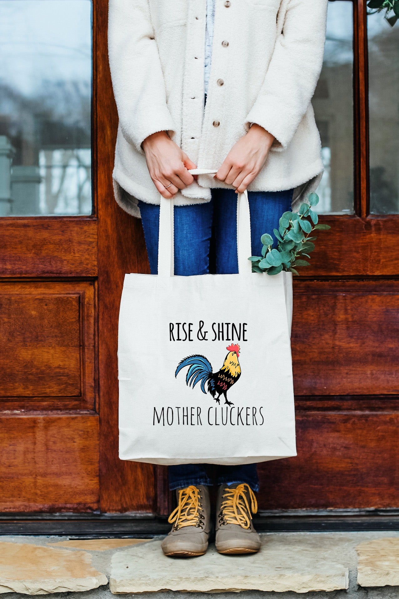 a woman holding a tote bag that says rise and shine mother cluckers