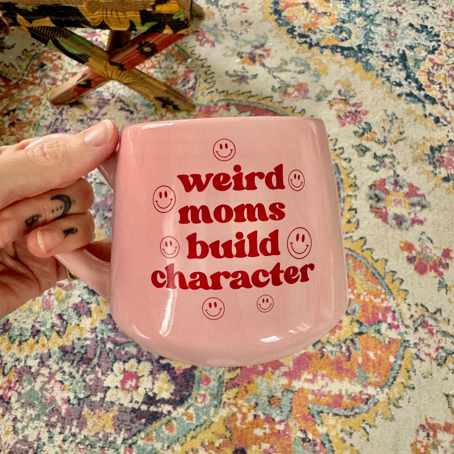 a person holding a pink coffee mug that says weird moms build character