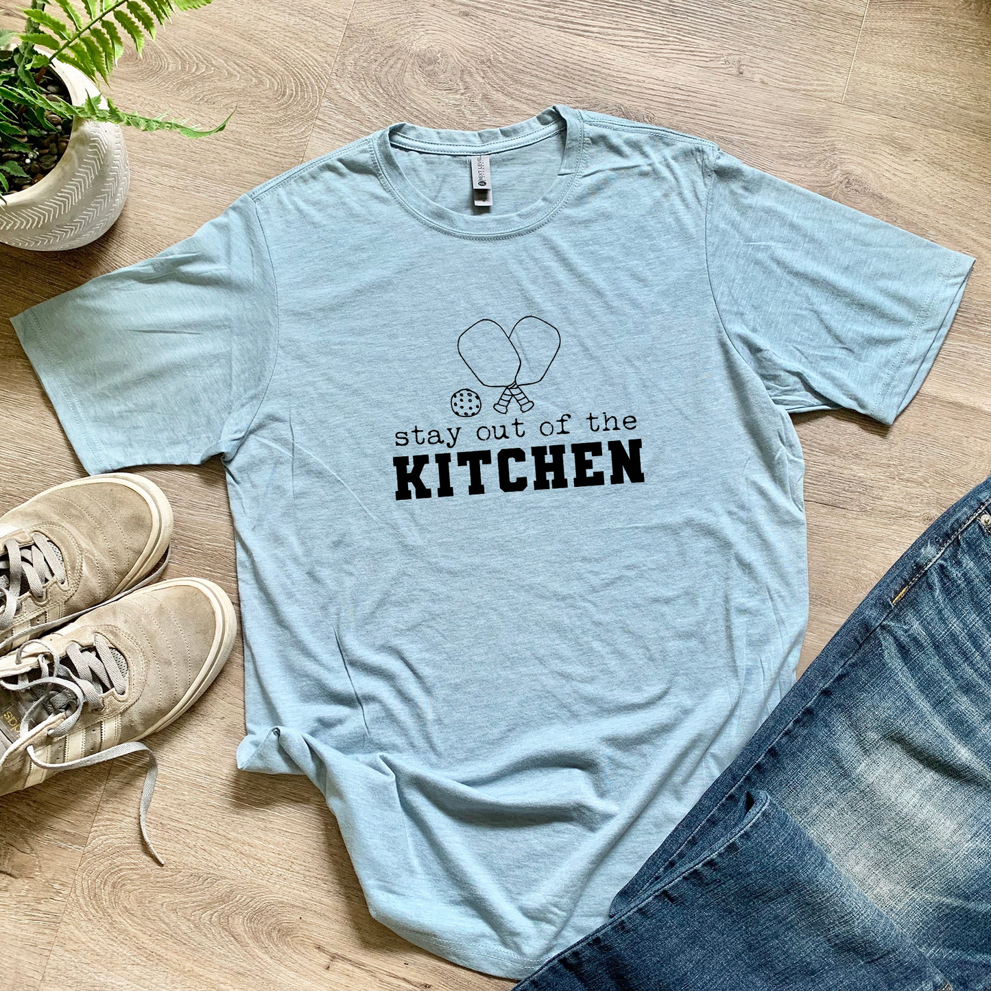 a t - shirt that says stay out of the kitchen next to a pair of