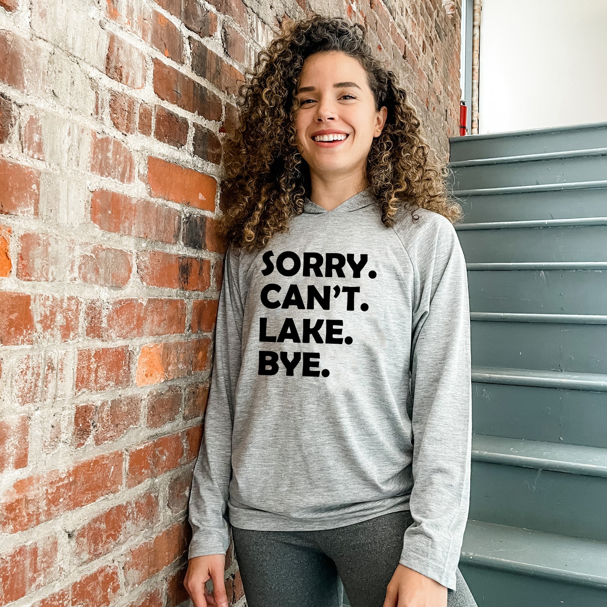 a woman leaning against a brick wall wearing a sweatshirt that says sorry can't