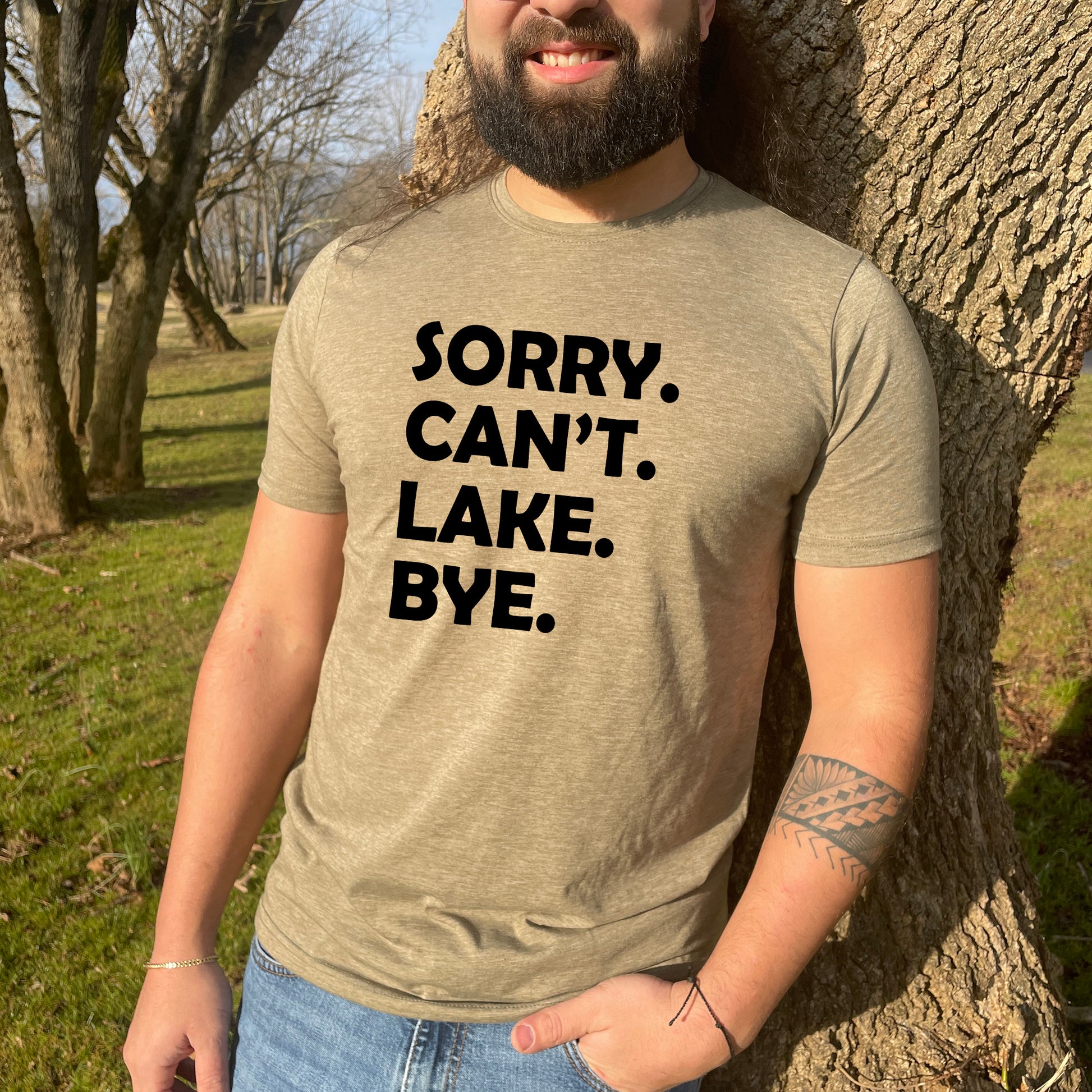 a man standing next to a tree wearing a shirt that says sorry can't