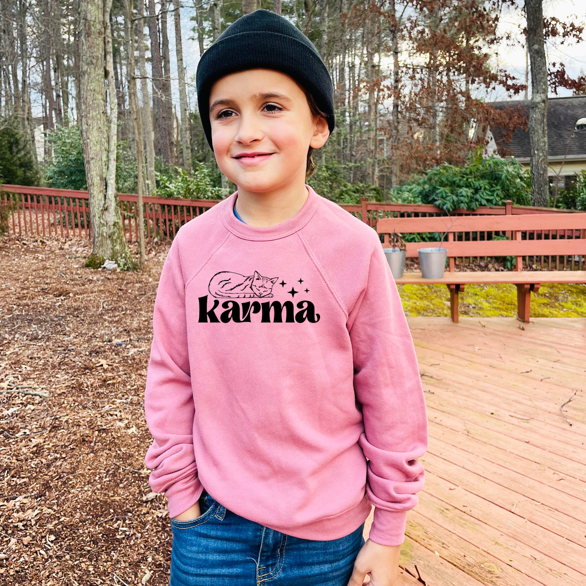 a young boy standing on a deck wearing a pink sweatshirt