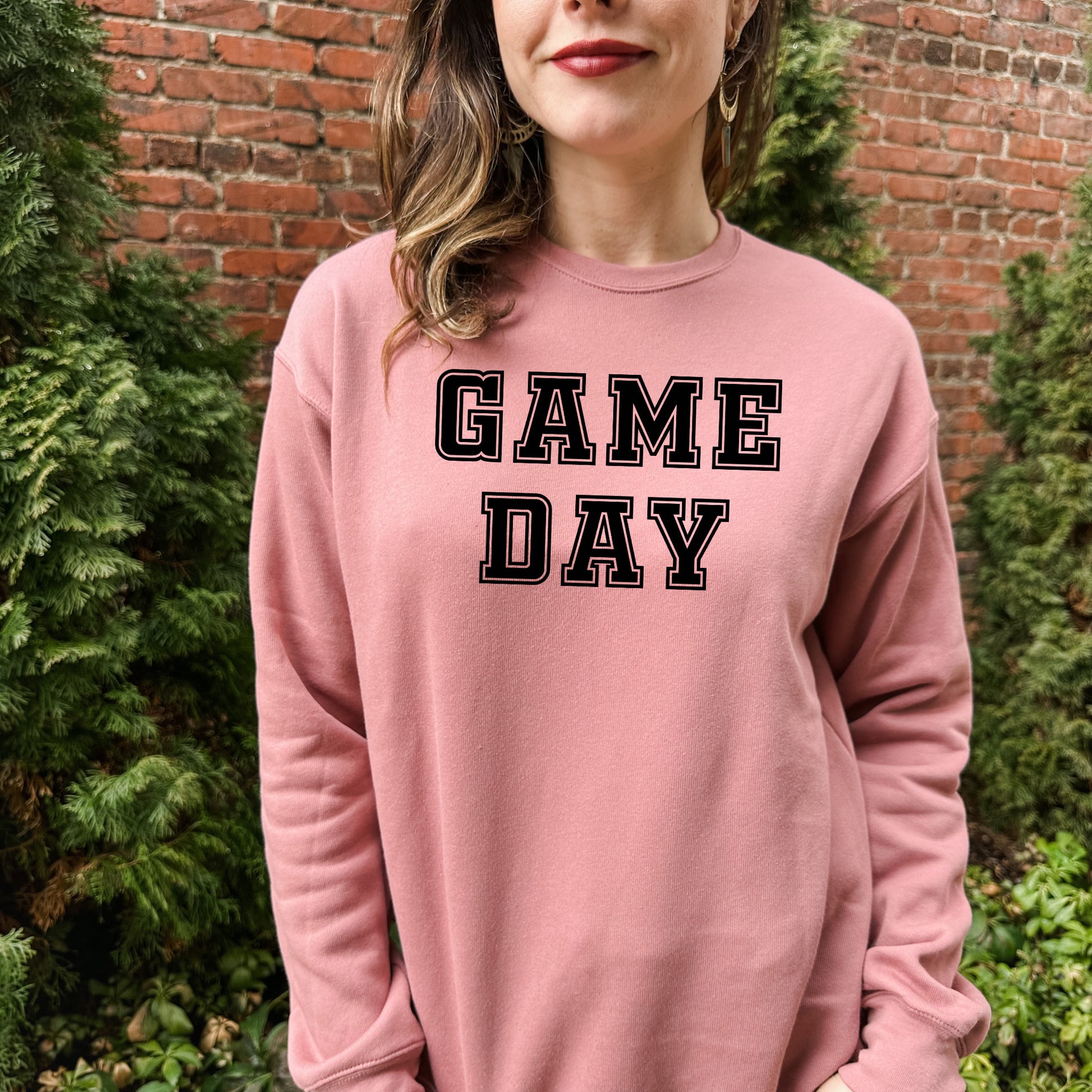 a woman standing in front of a brick wall wearing a game day sweatshirt