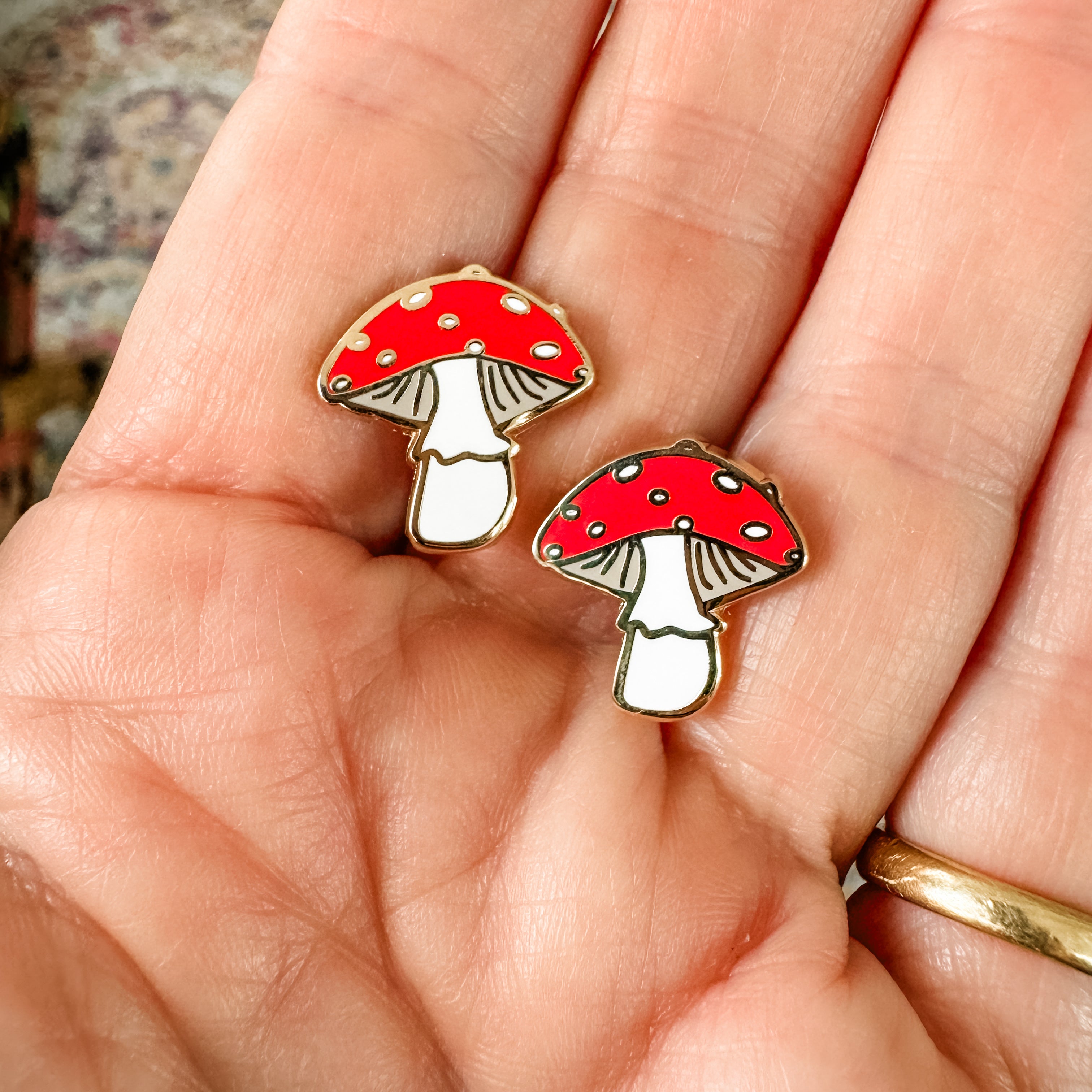 a hand holding two red and white mushrooms