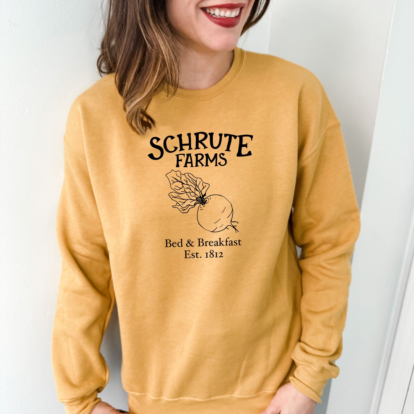 a woman wearing a yellow sweater with the words schrute farms on it