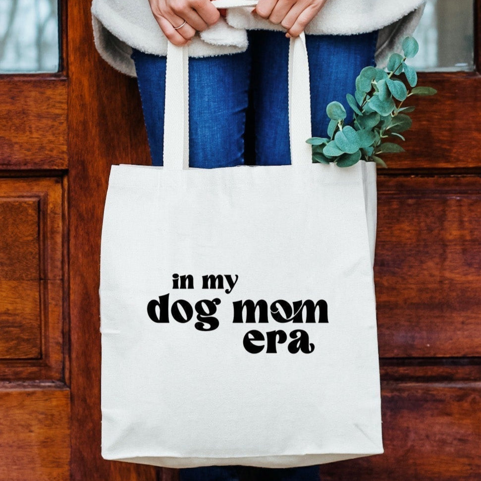 a woman holding a white bag that says in my dog mom era
