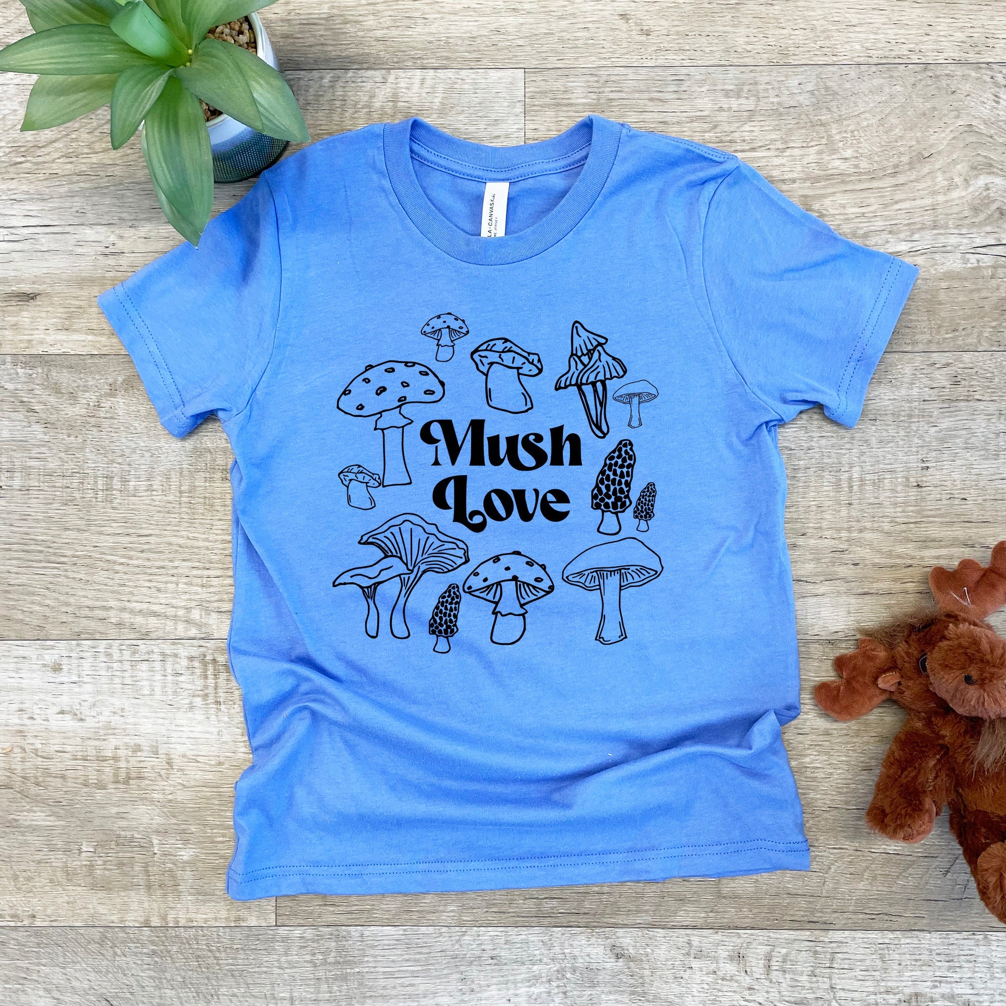 a blue t - shirt with mushrooms on it next to a teddy bear