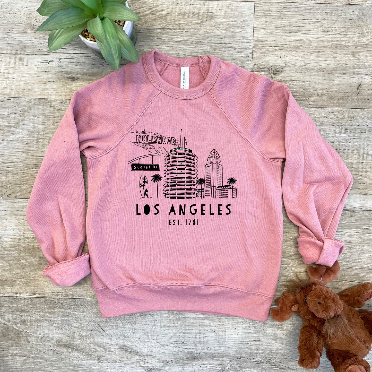 a pink sweatshirt with the los angeles skyline on it next to a teddy bear