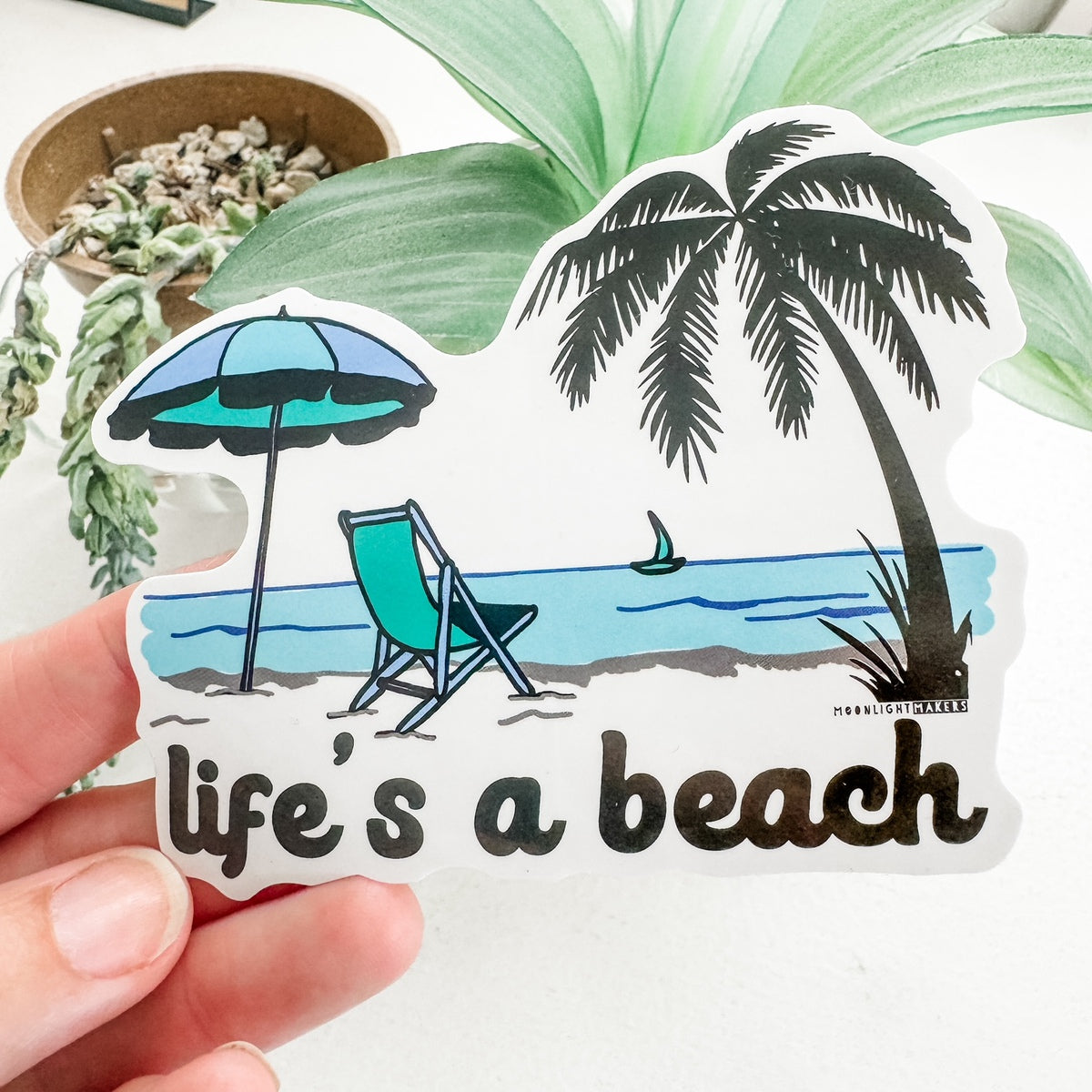 a hand holding a sticker that says life's a beach